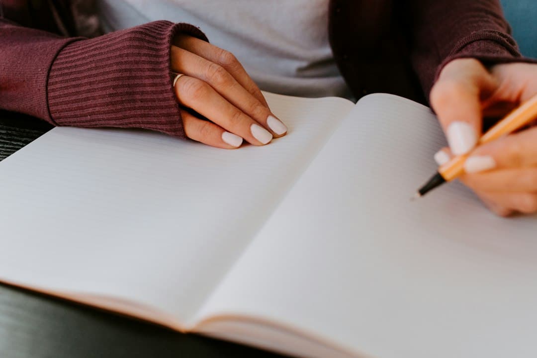 A woman's hands writing in a blank notebook at a desk