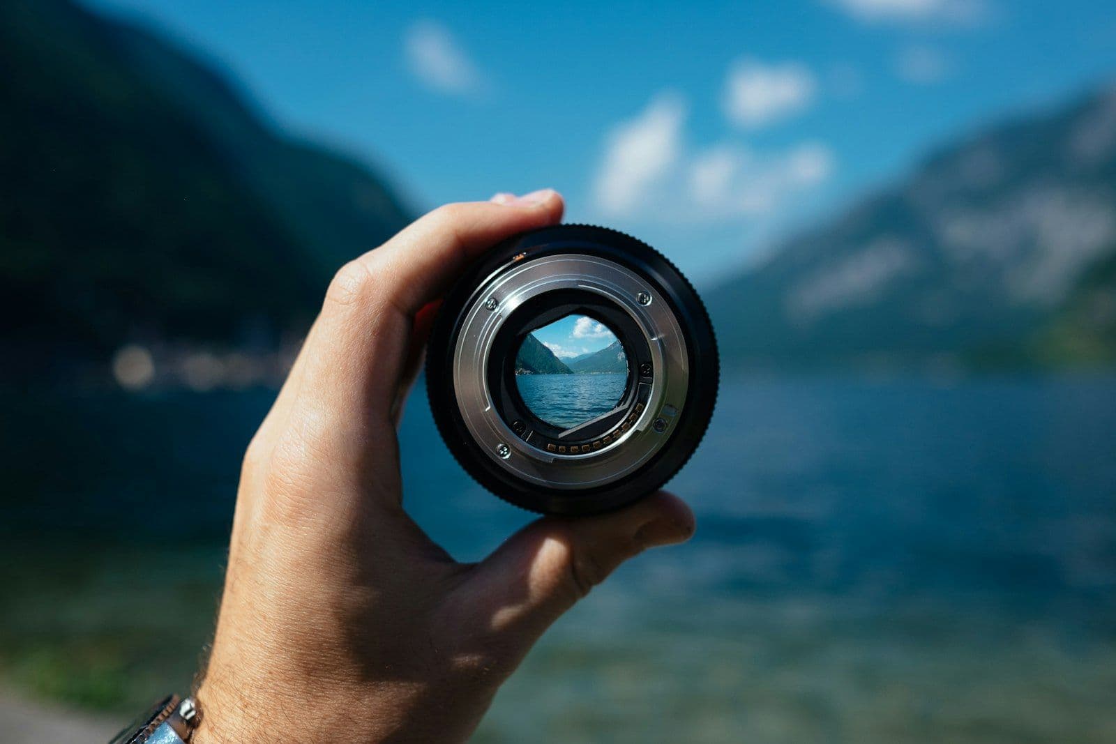 Une main tenant un objectif d'appareil photo qui cadre un paysage lointain