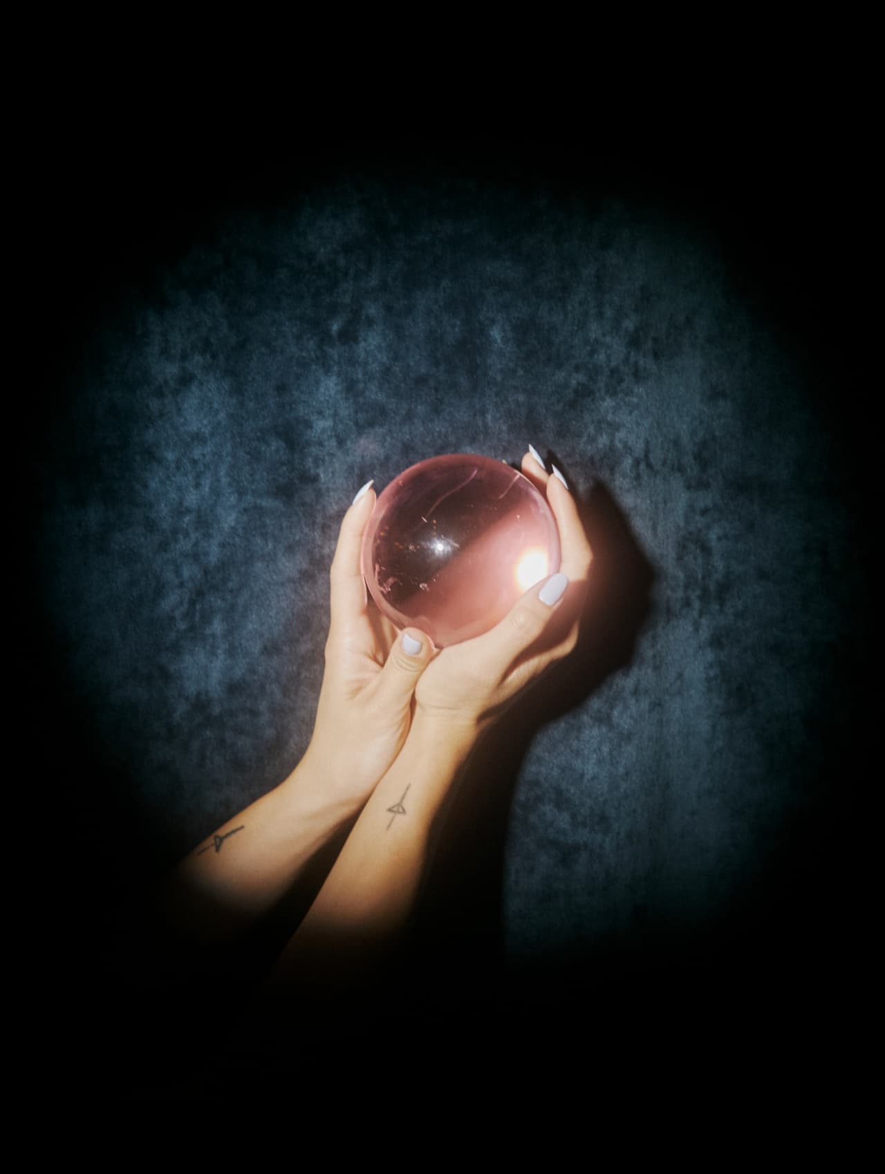 Two hands cupping a crystal ball against a mottled cloth backdrop, seen from above