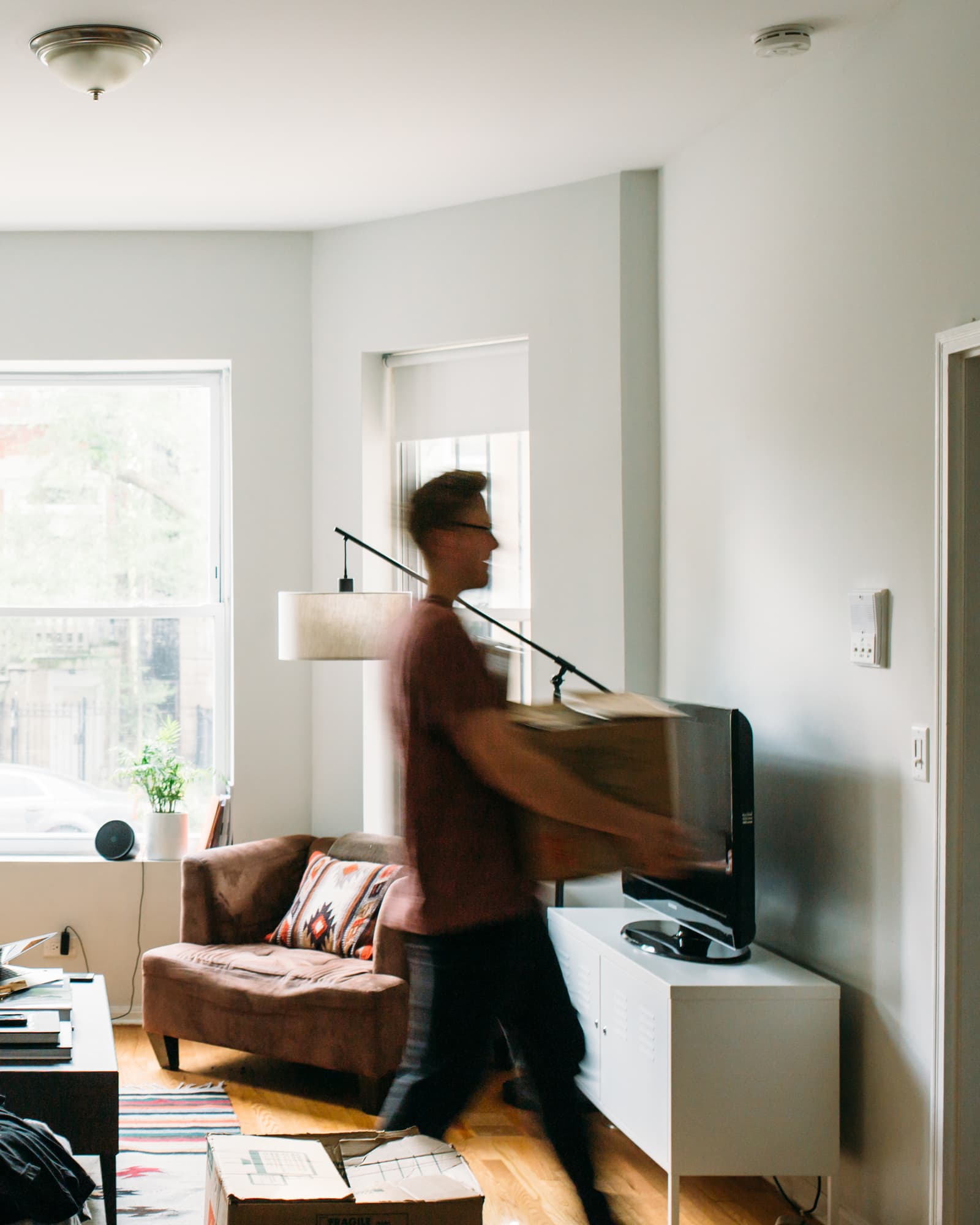 Person blurred in motion carrying a cardboard box through a living room, another box on the floor