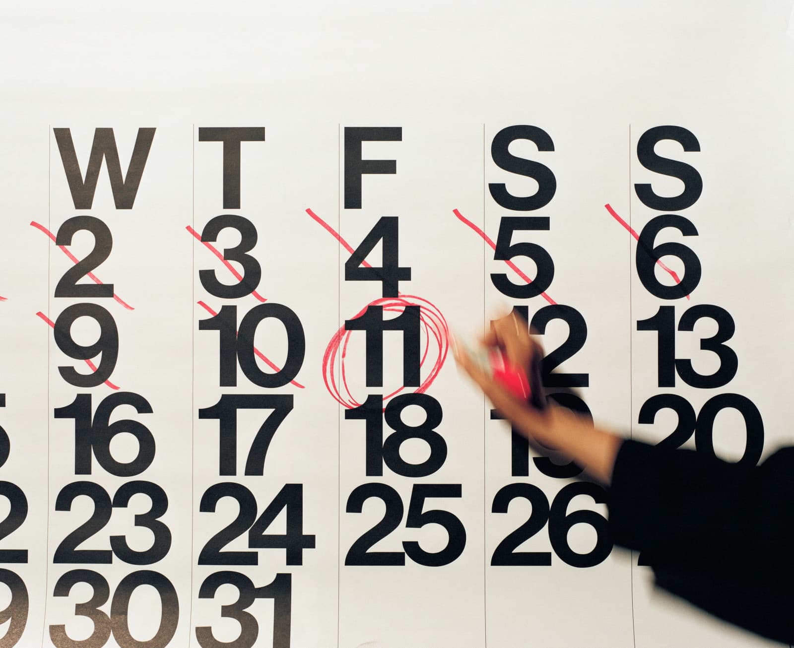 Hand with a red marker circling the 11th on a large wall calendar, earlier days crossed out